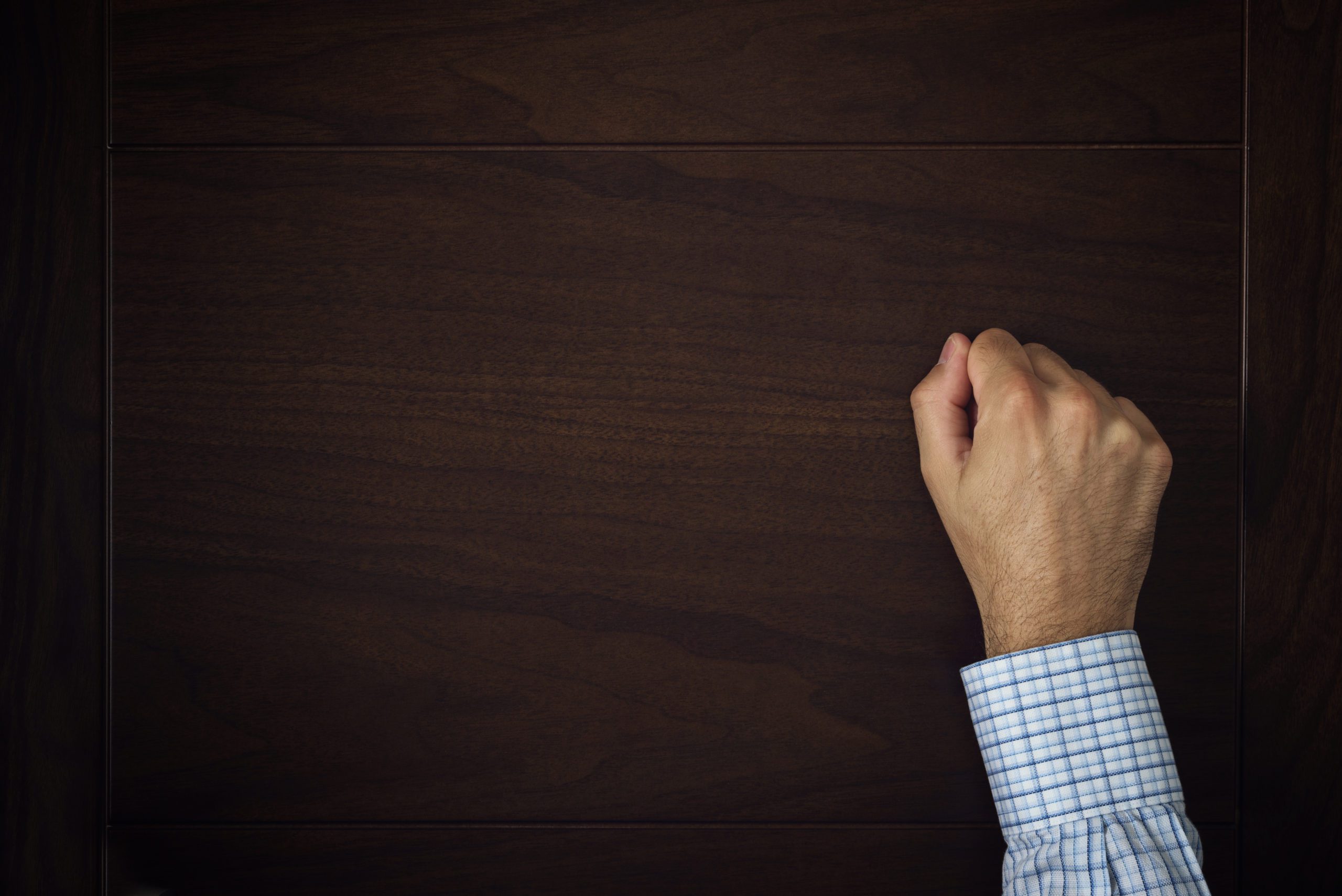 Hand Is Knocking On The Door Male hand is knocking on wooden door conceptual image. Visitor or guest is at the door.